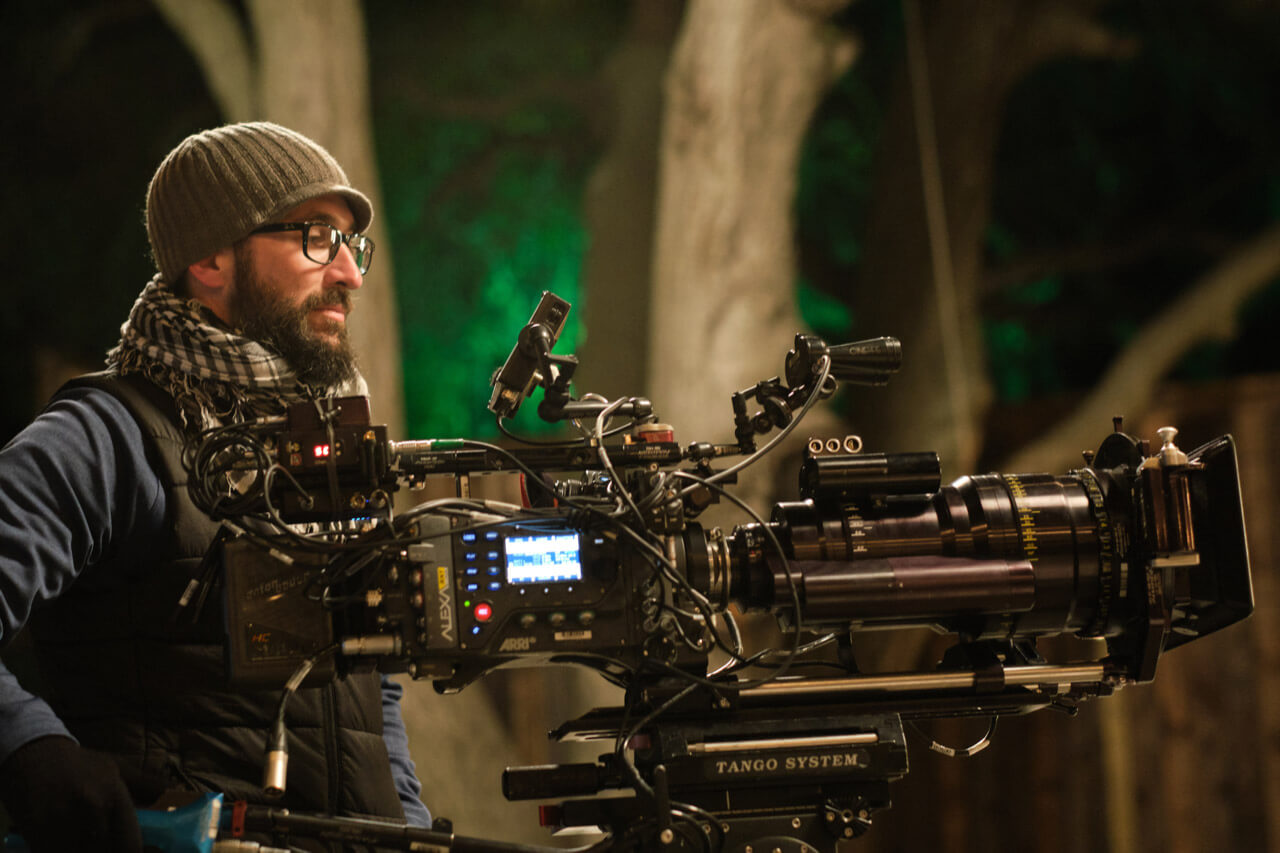 Andrew Aiello operating a video camera at night with lit trees in the background.